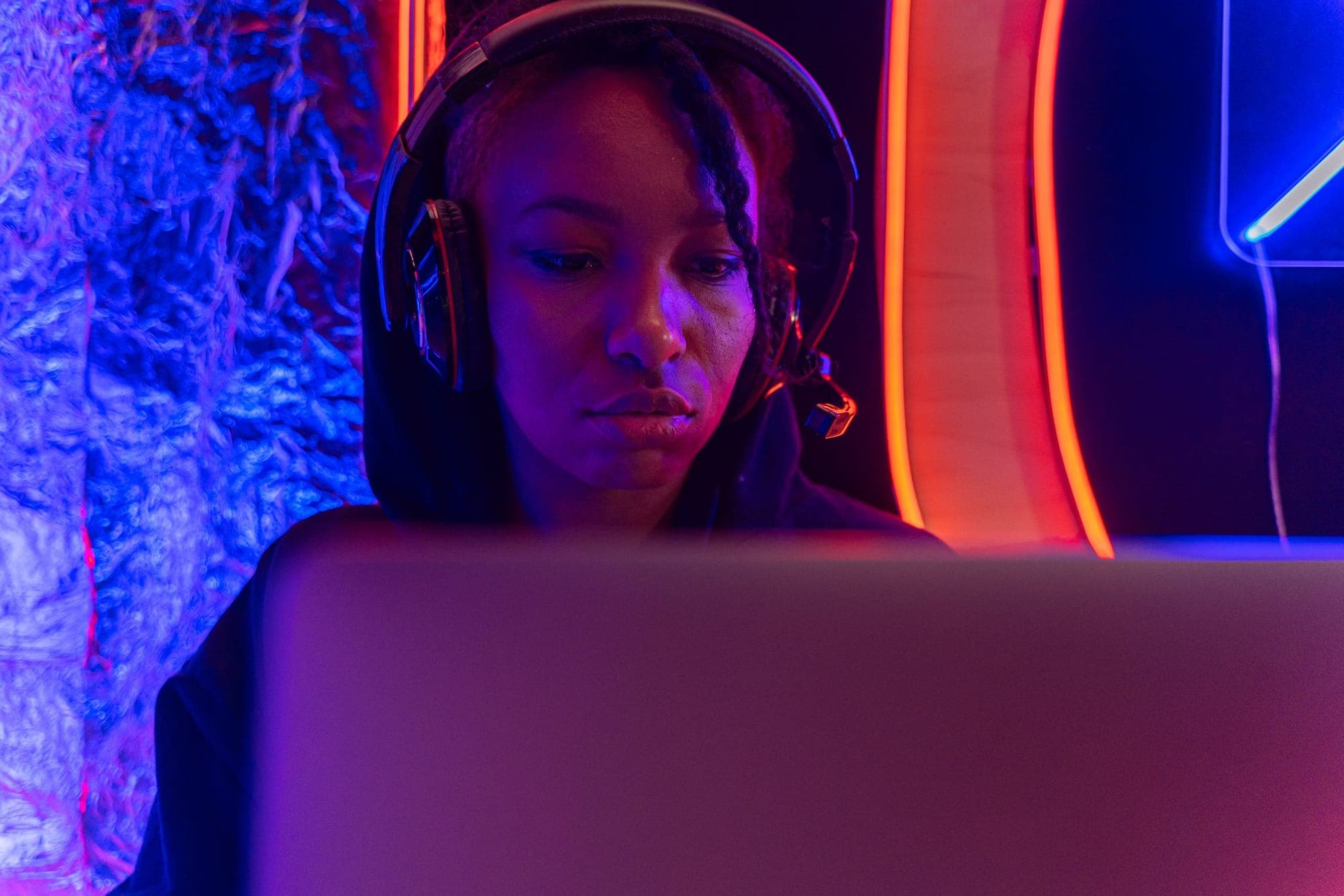 A woman wearing headphones at a laptop in a neon-lit room