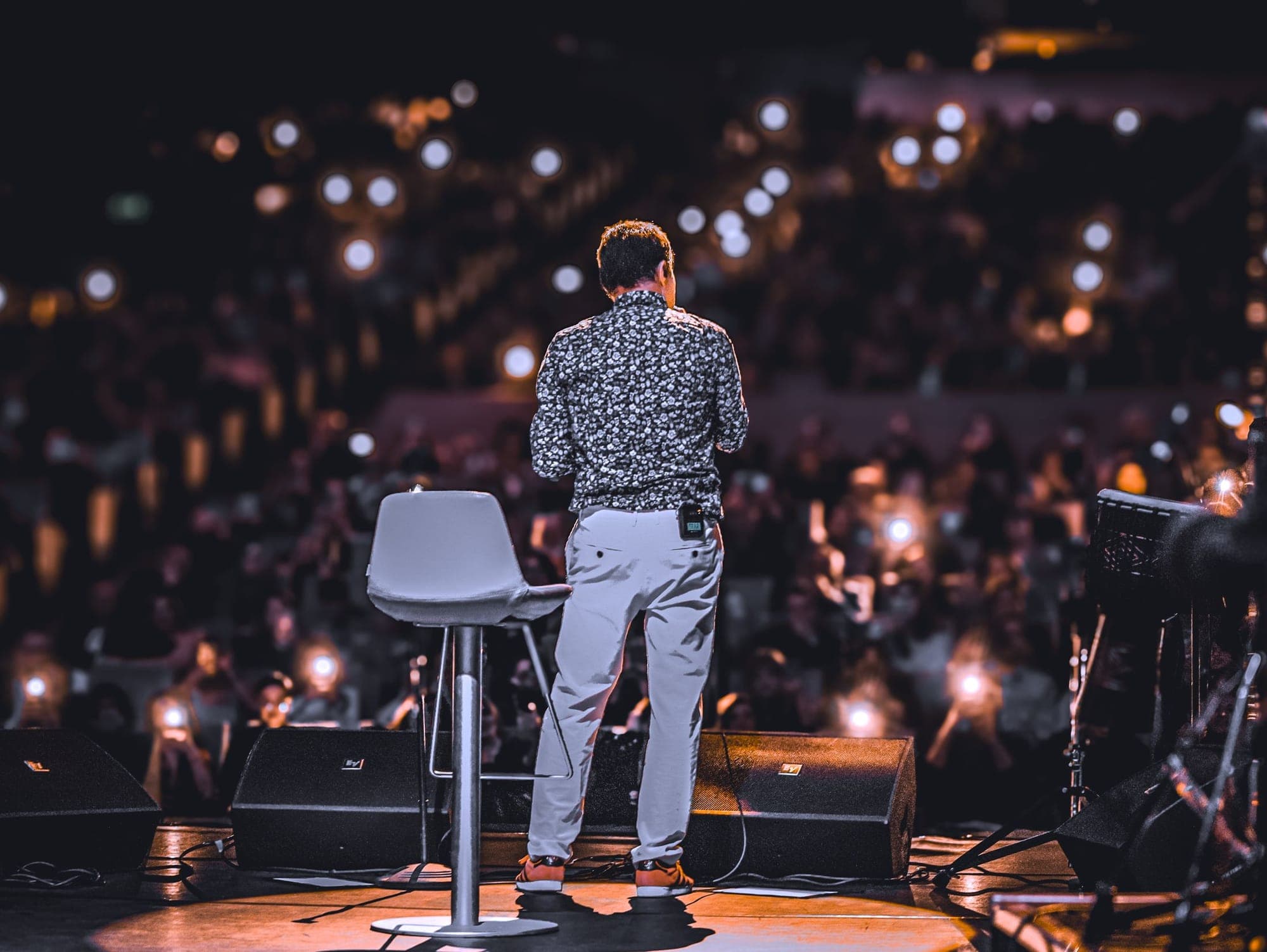 A speaker on stage facing an audience holding up phone lights