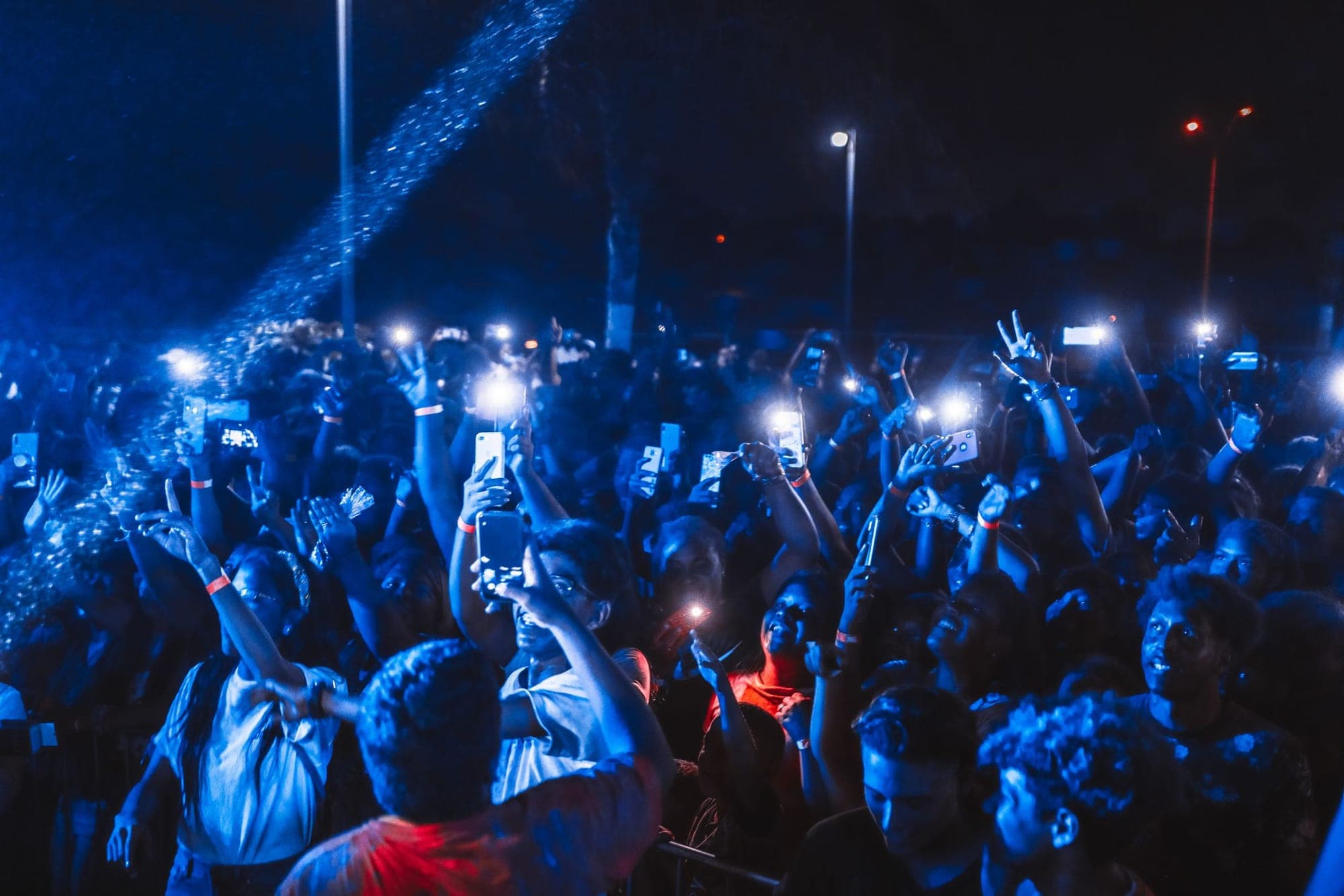 A crowd in blue light filming with their phones