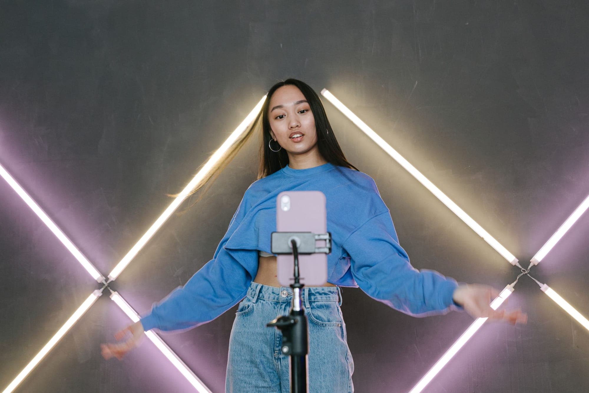 A creator dancing in front of a phone on a tripod under neon lights