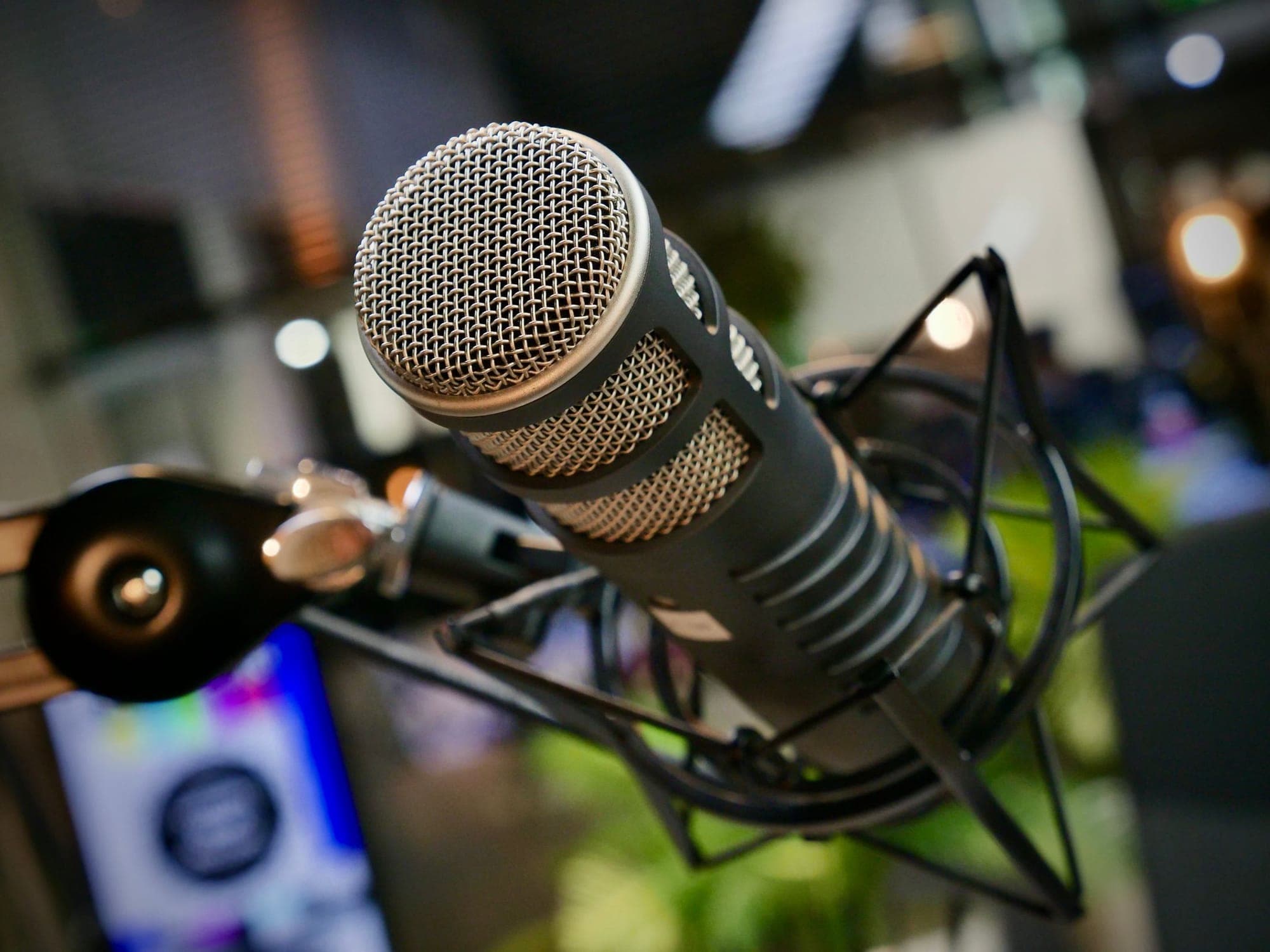 A podcast microphone on a desk arm in a dim studio